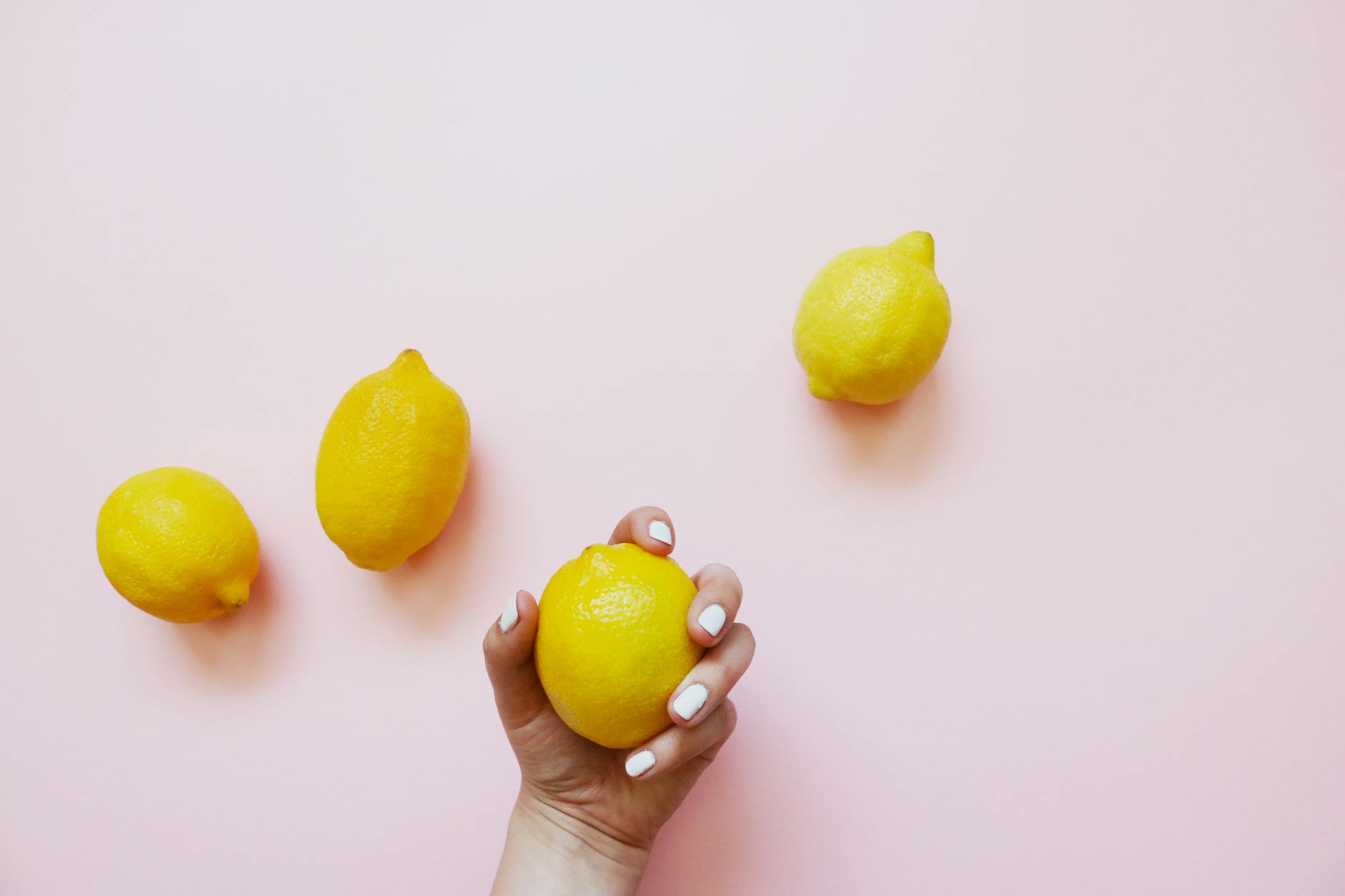 Hand holding a lemon against a soft pink background
