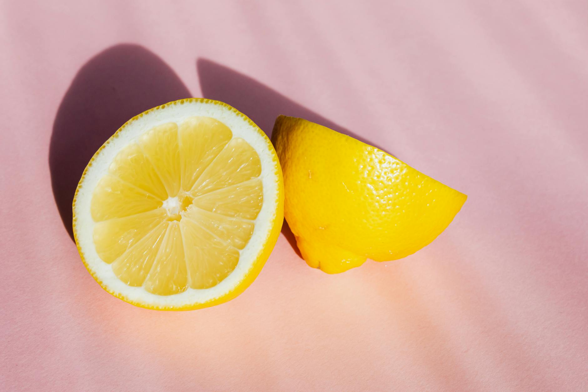 Hand holding fresh lemon on soft pink background with allergy-friendly elements
