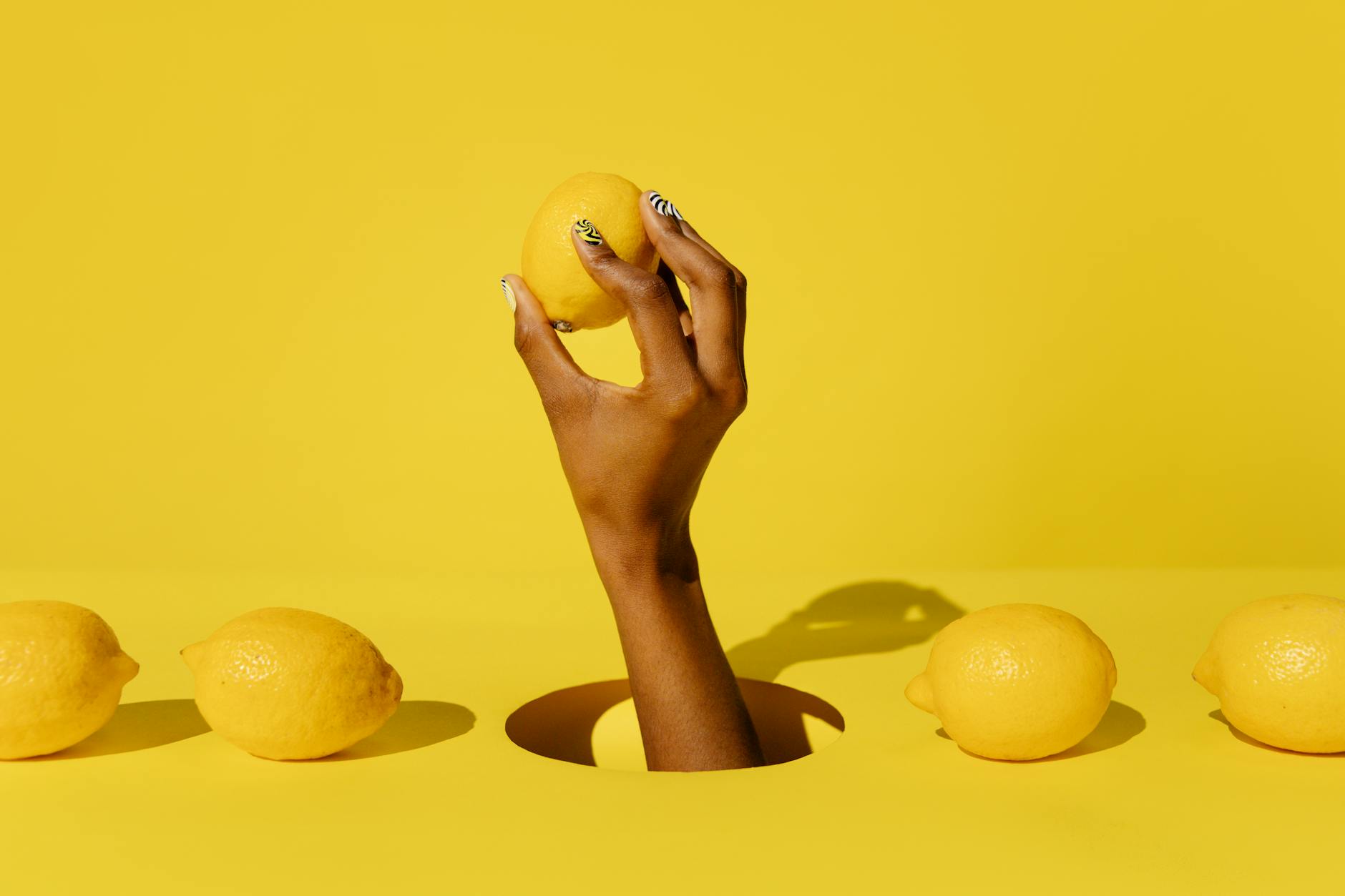 Hand holding a fresh lemon against a vivid yellow background, symbolizing natural pleasure and vitality