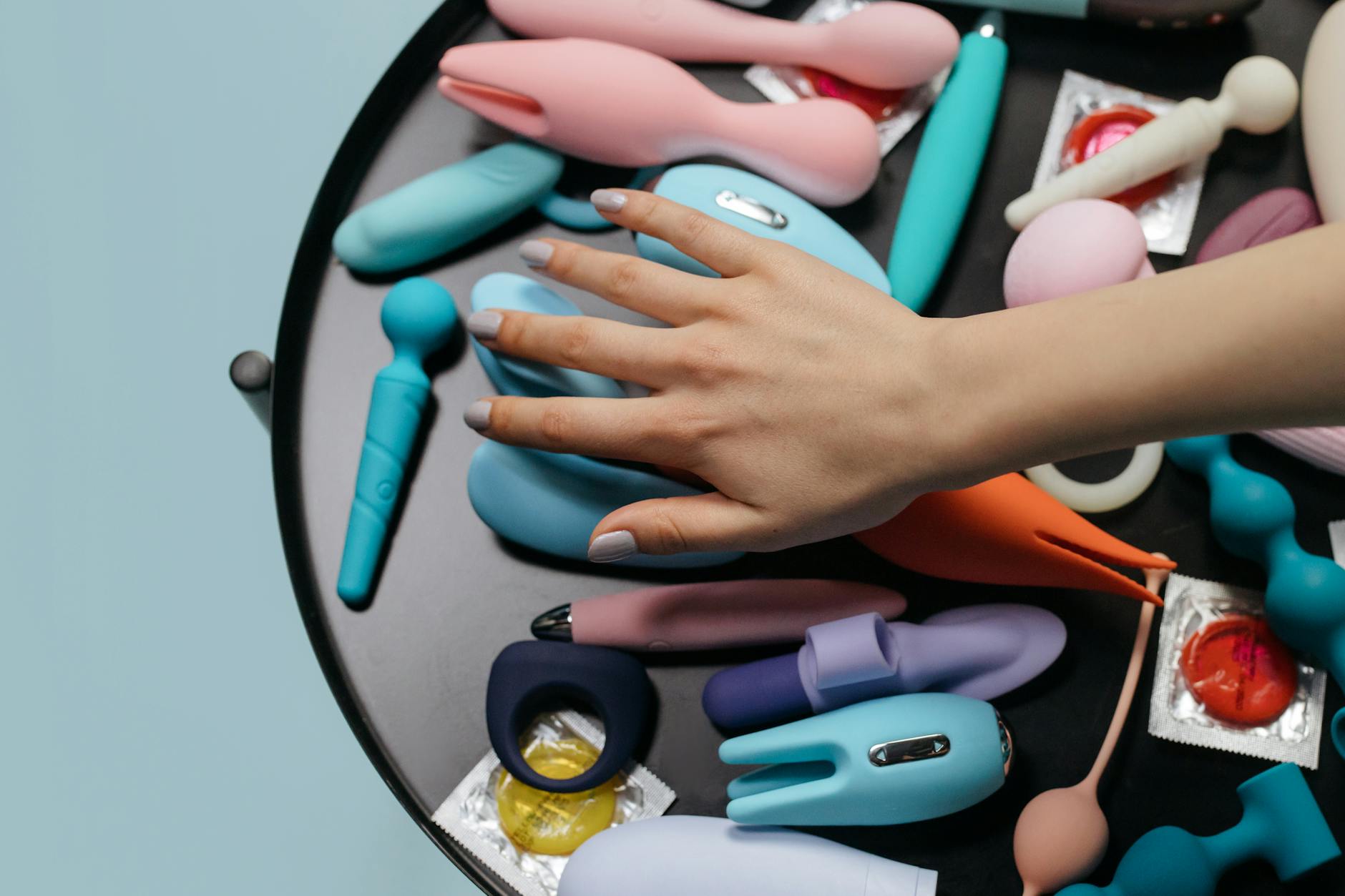 A hand reaching over a variety of colorful lemon vibrators and adult toys arranged on a table.