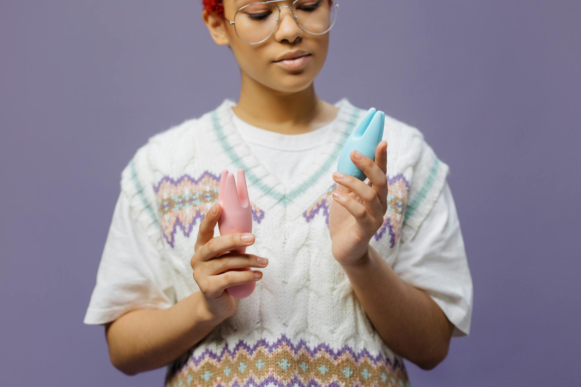 Woman in eyeglasses thoughtfully holding a pink silicone vibrator, contemplating sexual wellness.