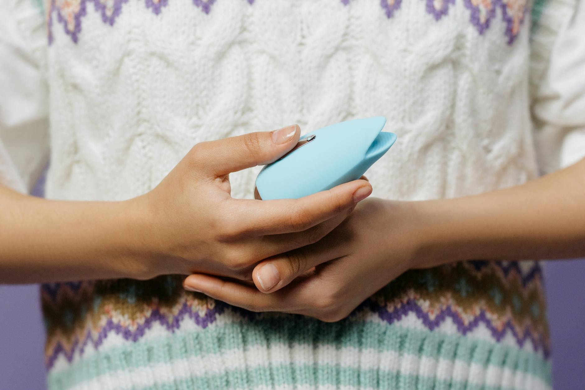 Close-up of hands holding a blue lemon clitoral vibrator against a knitted sweater.