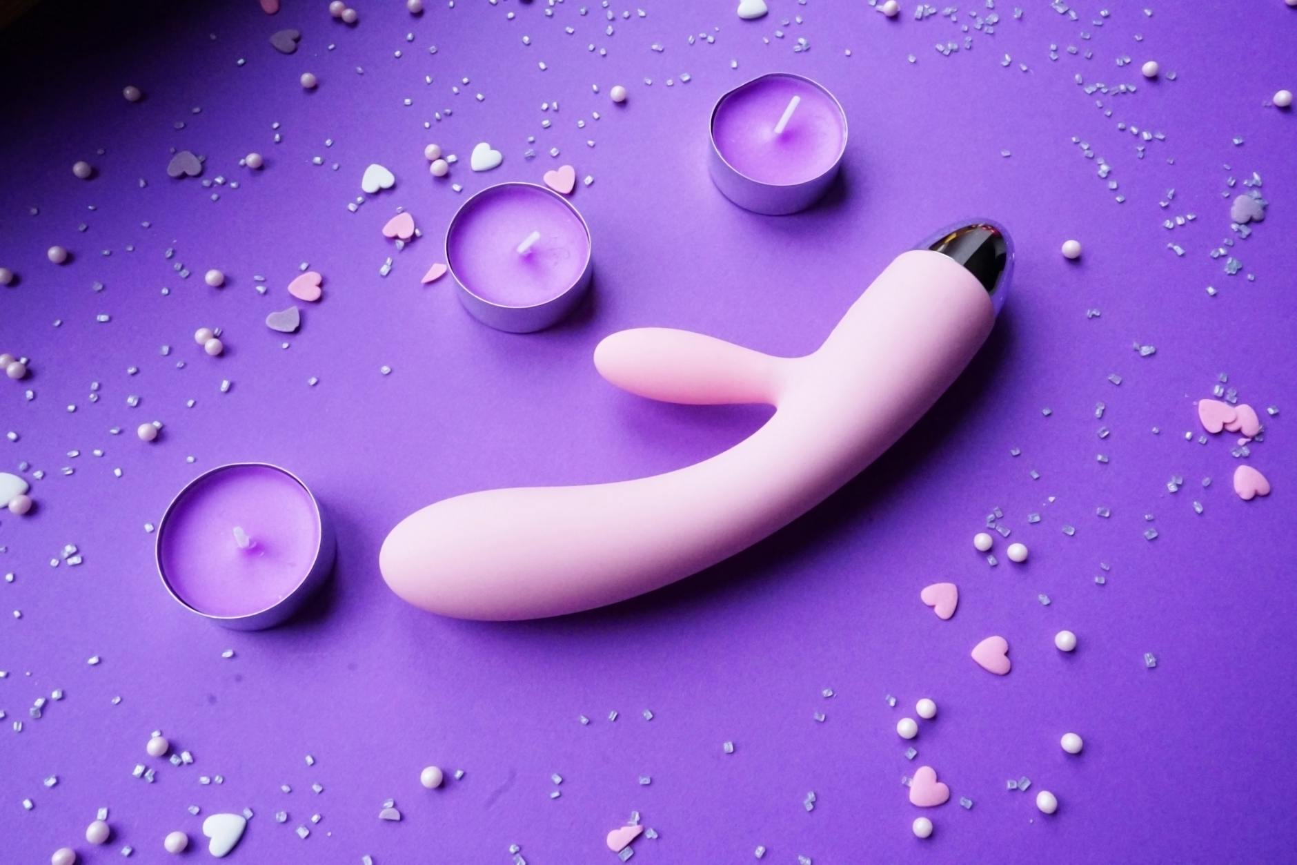 Pink vibrator on purple background with heart confetti and candles for romantic setting